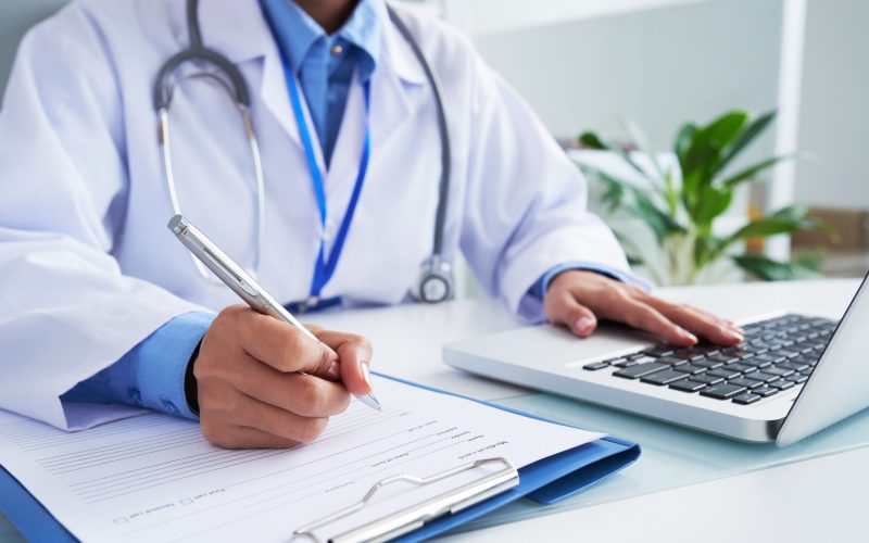 Doctor checking information in computer program before filling medical card