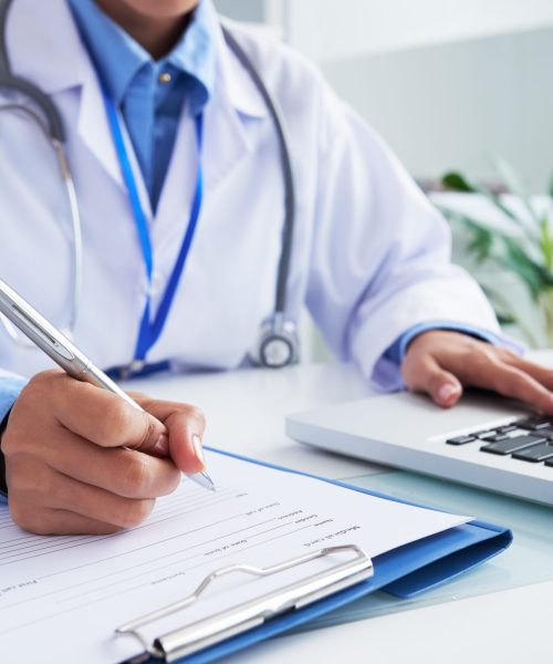 Doctor checking information in computer program before filling medical card